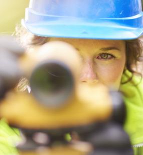 A female surveyor looks through a theodolite into the camera