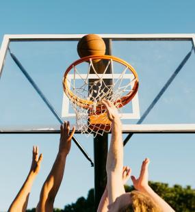 hands reaching towards a basketball hoop and ball