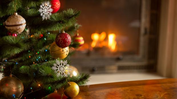 A close-up of a Christmas tree decorated with gold and red baubles in front of an open fire