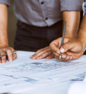 Two planning consultants lean over blueprints laid out on a desk